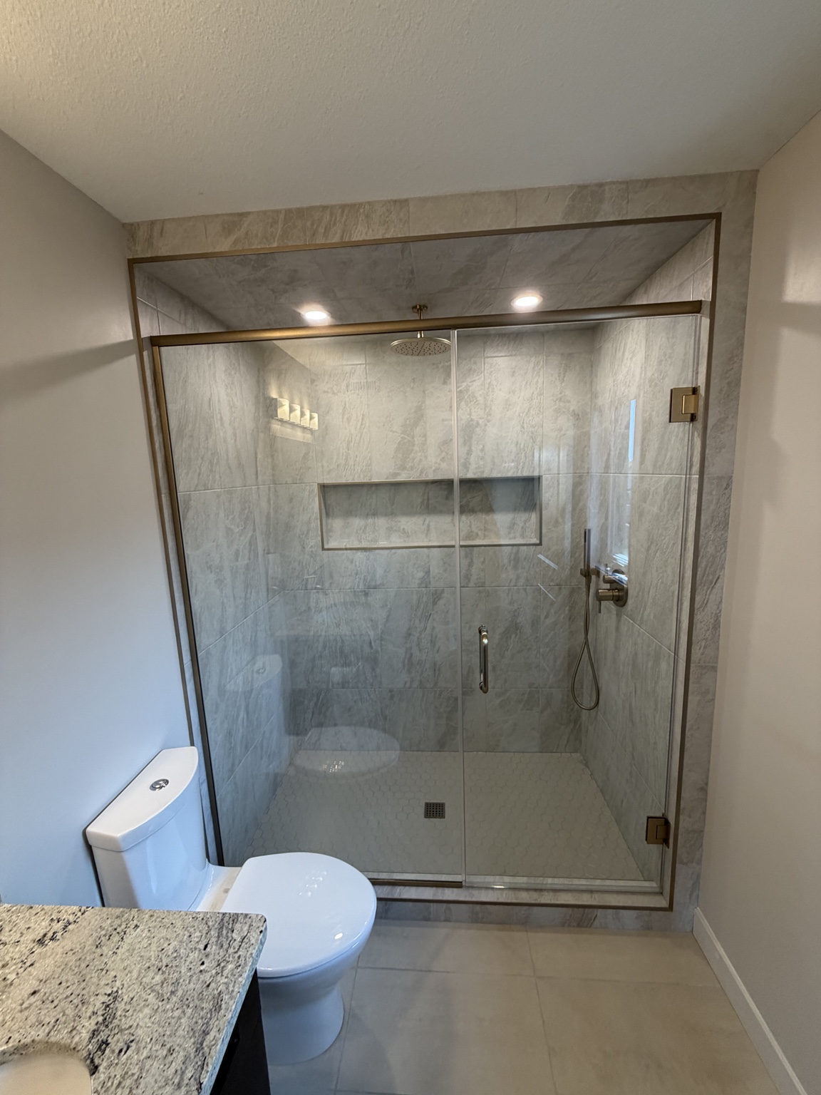 Finished tiled shower with glass enclosure and brass-tone fittings